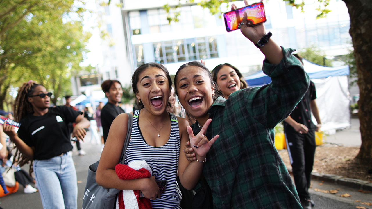 Two students in Alfred Street, Central Auckland. One student is waving and holding a mobile phone.