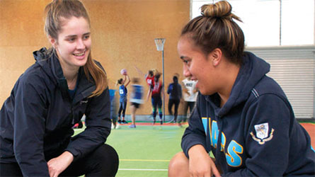 Two students crouching and talking on an indoor court