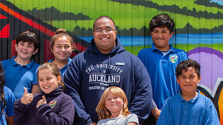 A group of mixed age people smiling as they stand against a green wall.