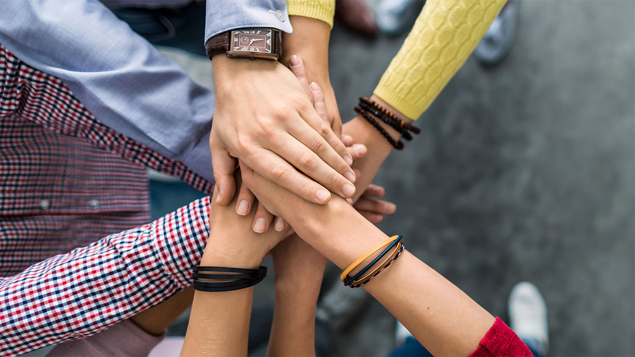 A circle of clasped hands, viewed from above.