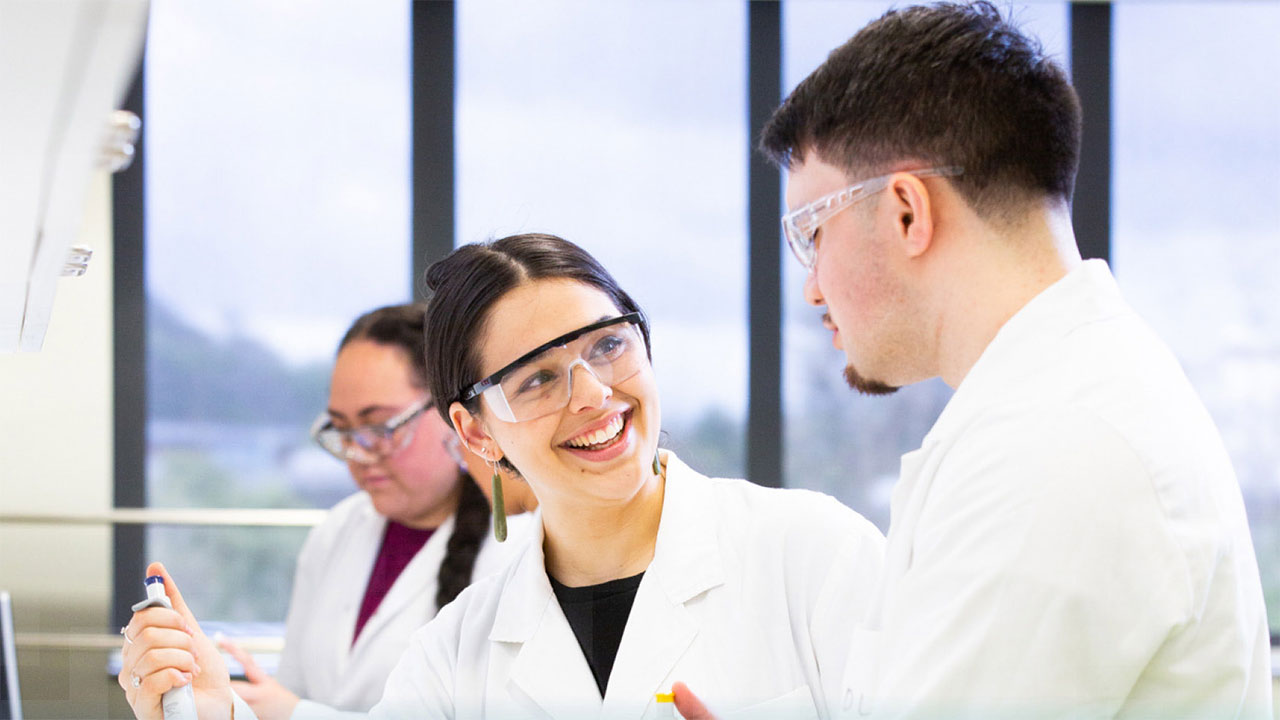 Smiling students in lab coats working on an experiment.