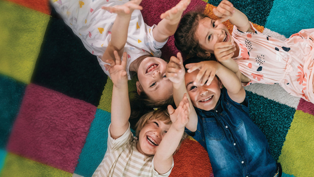 Happy young children lying on a colourful rug.