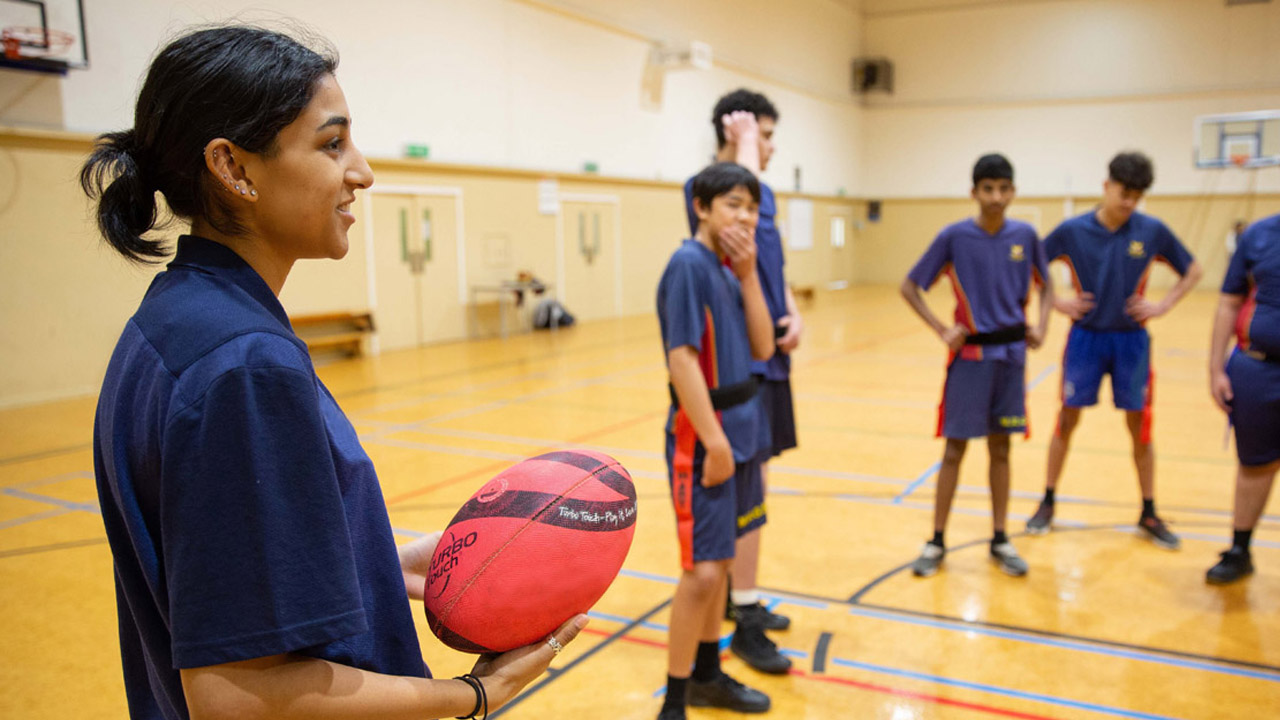 Young teacher inside a gymnasium talking to a group of boys.