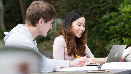Group of students working together outside on a laptop.