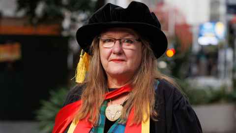 A bespectacled woman smiling at the camera in her doctoral regalia. 